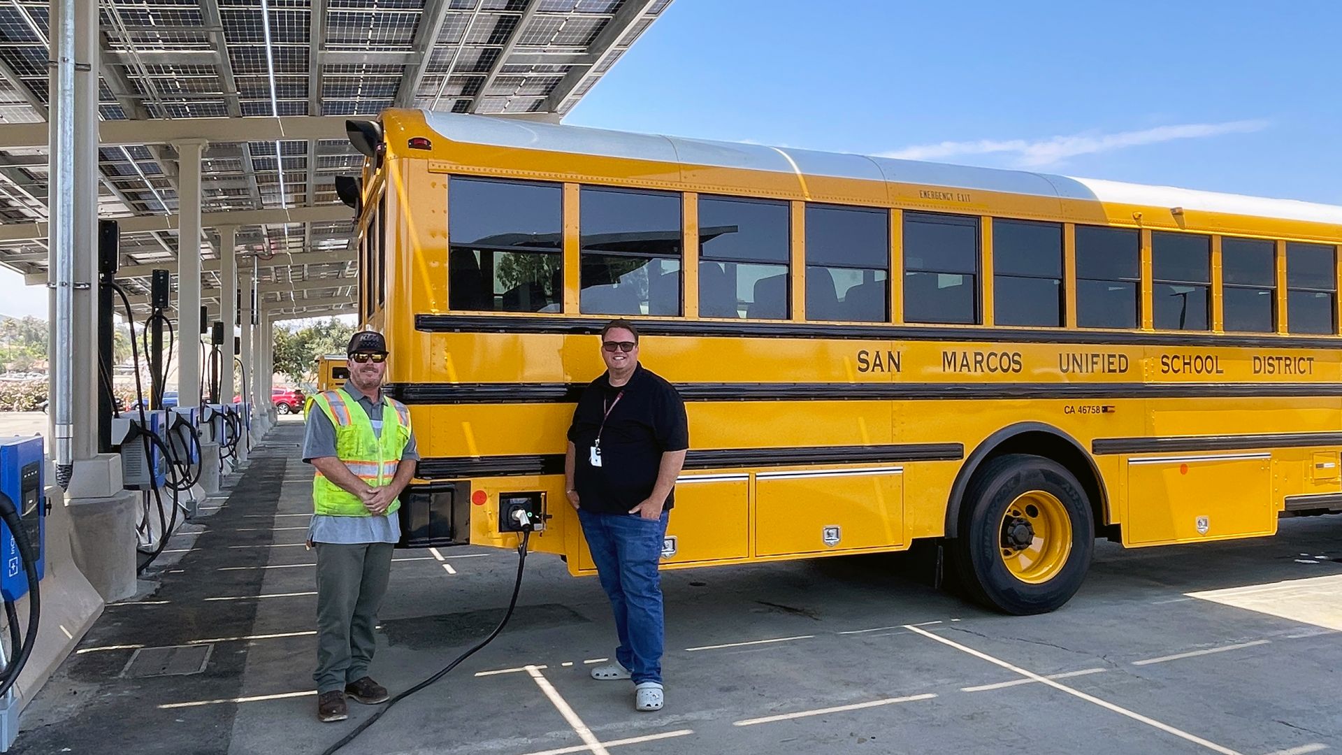 Electric school buses charging under solar panel canopies at a San Marcos Unified School District facility.